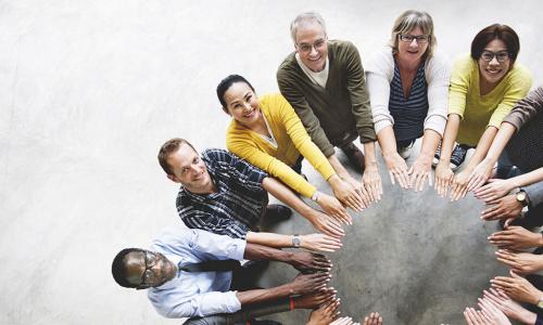 diverse group of happy people putting their hands into the center to form a circle