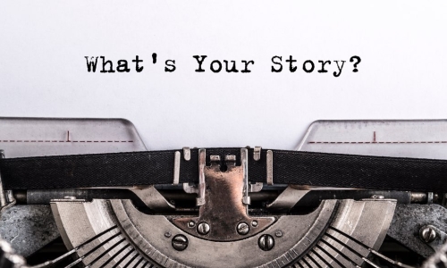 The text What’s Your Story typed on paper above a typewriter