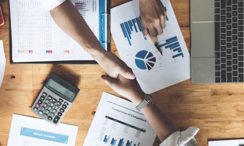 overhead shot of handshake over a table with financial charts