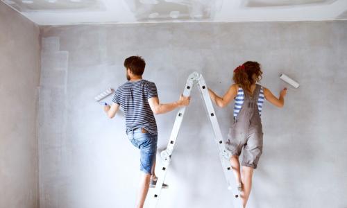 young couple on a ladder painting walls of new house