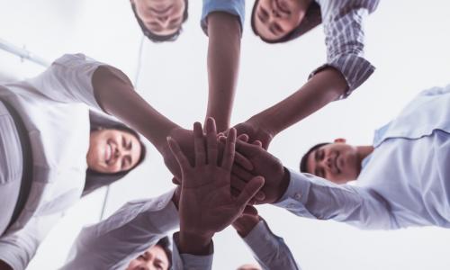 circle of businesspeople putting their hands together in the middle to signify teamwork and support