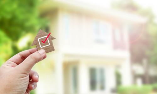 wooden house with red checkmark and a real house in the background