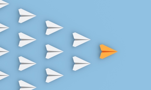 orange paper airplane leading a group of white paper airplanes in formation