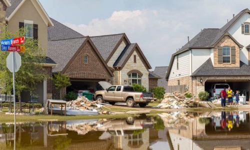 two homes rebuilding with flooding and a man in a yellow emergency worker vest