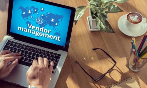 person reviewing vendor management chart on laptop sitting on wooden desk