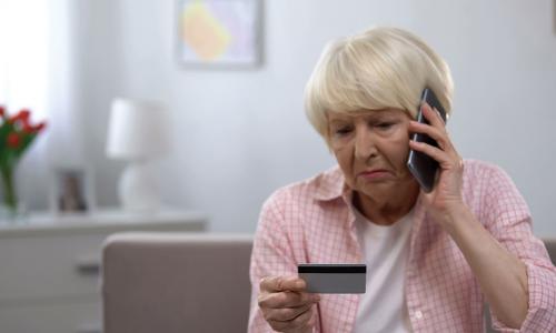 upset elderly woman on phone looking at credit card