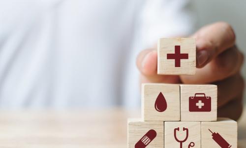 hand stacking wooden blocks with symbols representing health care and insurance