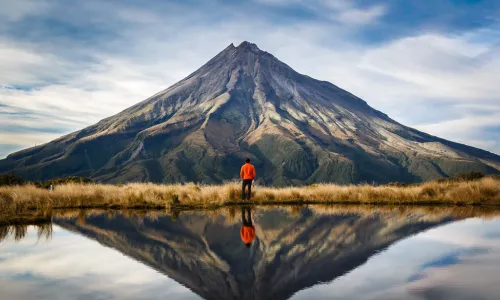 mountaineer looking at mountain with reflection of mountain behind in lake