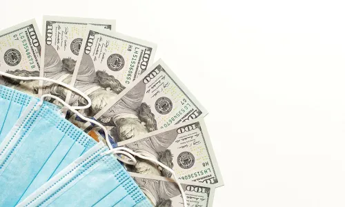 blue disposable face masks fanned out over 100 dollar bills