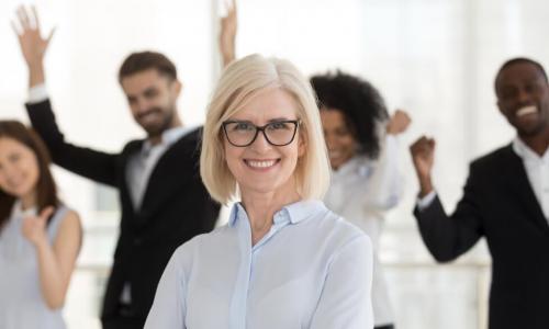 smiling female executive with team celebrating behind her