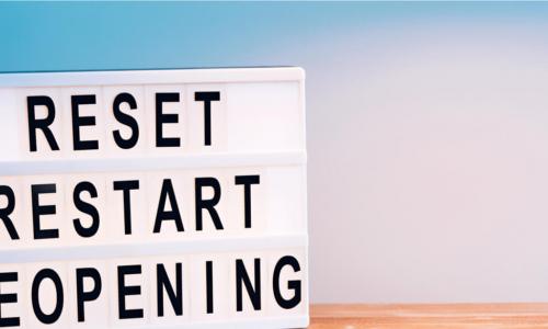 reset restart reopening sign on wooden table in front of blue background