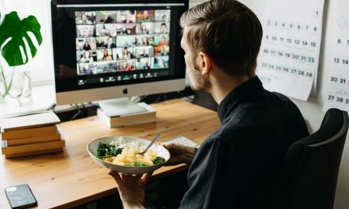 man eating lunch while meeting with colleagues virtually