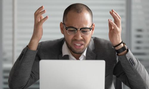 stressed businessman gestures angrily at laptop screen