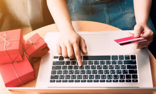 woman with red presents alongside her pays with credit card using laptop