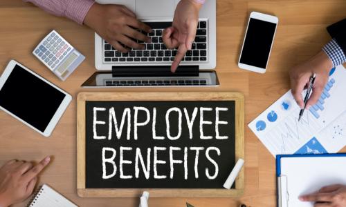 employee benefits written on small chalkboard on a table with three employees working at it