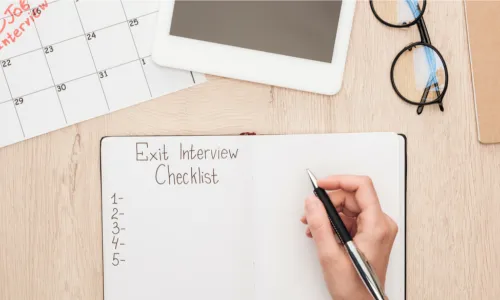 partial view of recruiter holding pen near notebook with exit interview checklist lettering
