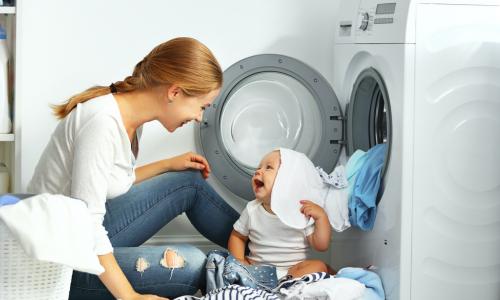 mother a housewife with a baby engaged in laundry fold clothes into the washing machine