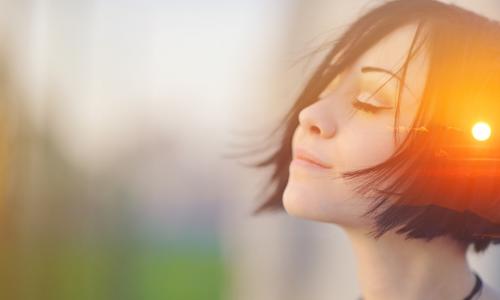 sunset superimposed on image of woman with eyes closed taking deep meditative breath to release stress