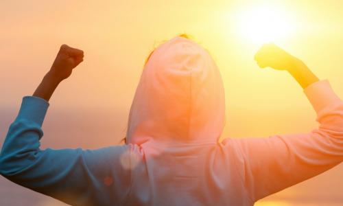 Back view of strong motivated woman celebrating goals towards the sun