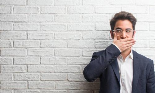 man covering mouth with hand standing by white wall