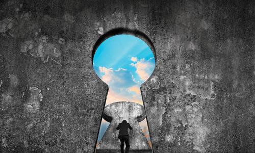 businessman pushing open a giant keyhole in a stone wall to reveal blue sky
