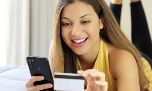 woman laying on a bed using credit card and smart phone