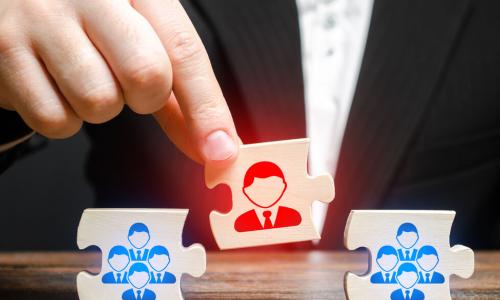 businessperson placing a red puzzle piece representing a leader between blue puzzle pieces representing employee team