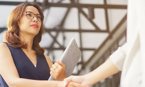 serious looking Asian businesswoman holding a portfolio shakes hands with vendor