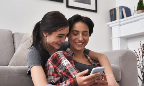 lesbian couple sitting in front of couch using smartphone