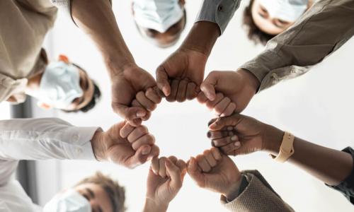 engaged group of masked employees bumping fists in a circle