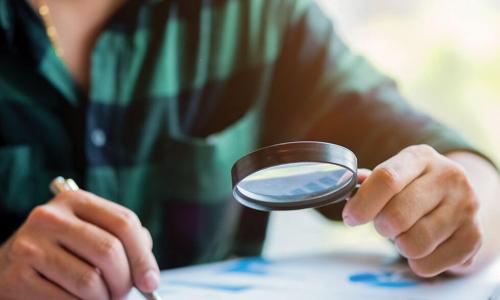 person in green plaid shirt examines report with a magnifying glass