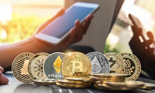 hand holding smartphone next to laptop keyboard covered in cryptocurrency coins