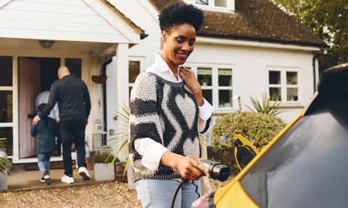 woman charges electric vehicle while husband and son enter the front door of new home