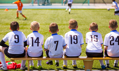 children's sports team sitting on the bench watching the game